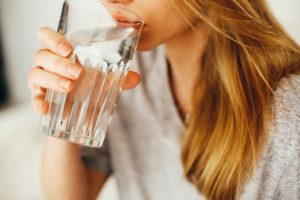 women in gray shirt drinking a large glass of water